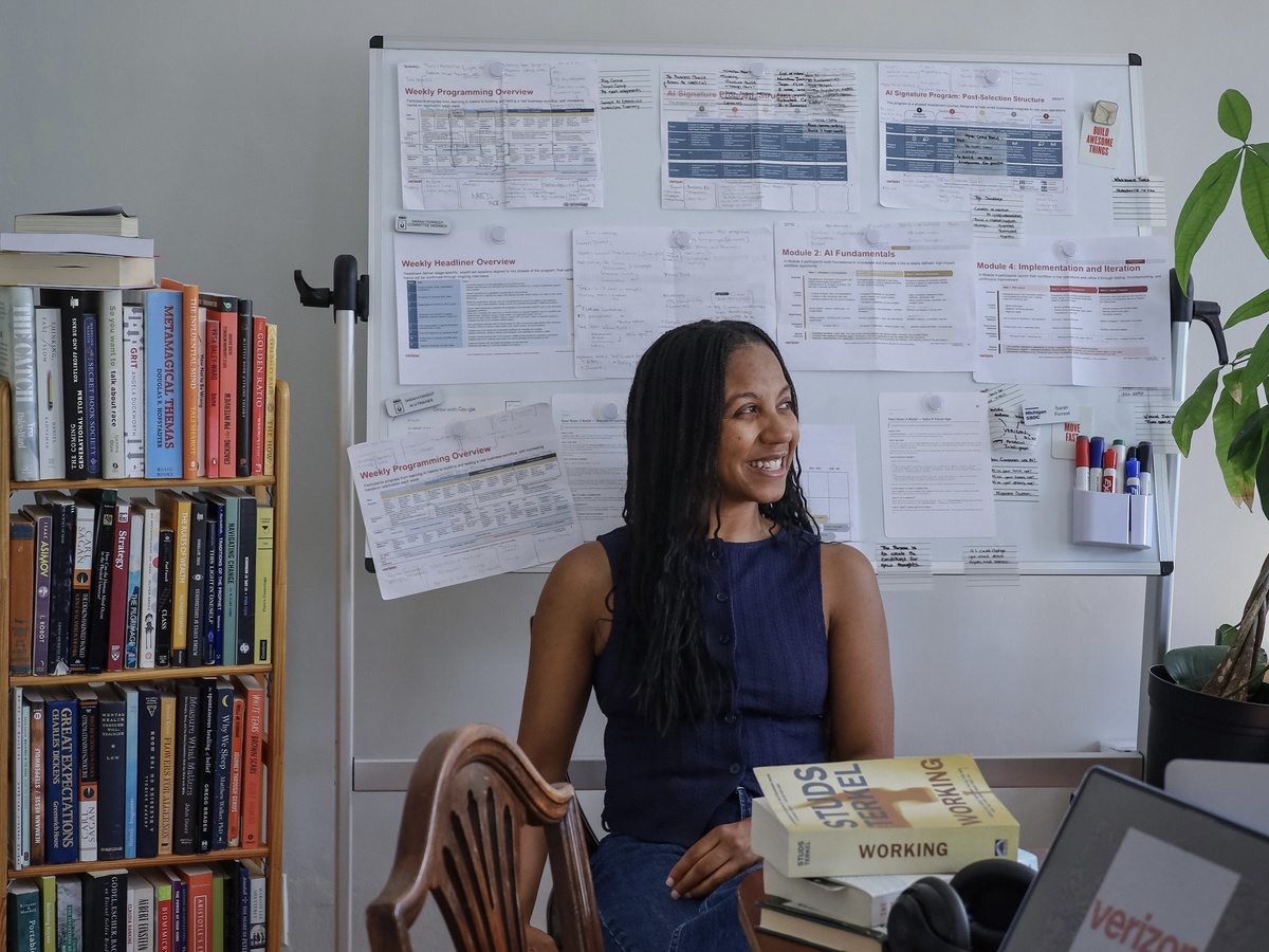 Sarah Forrest in a workspace with a whiteboard, books, laptop, and program materials